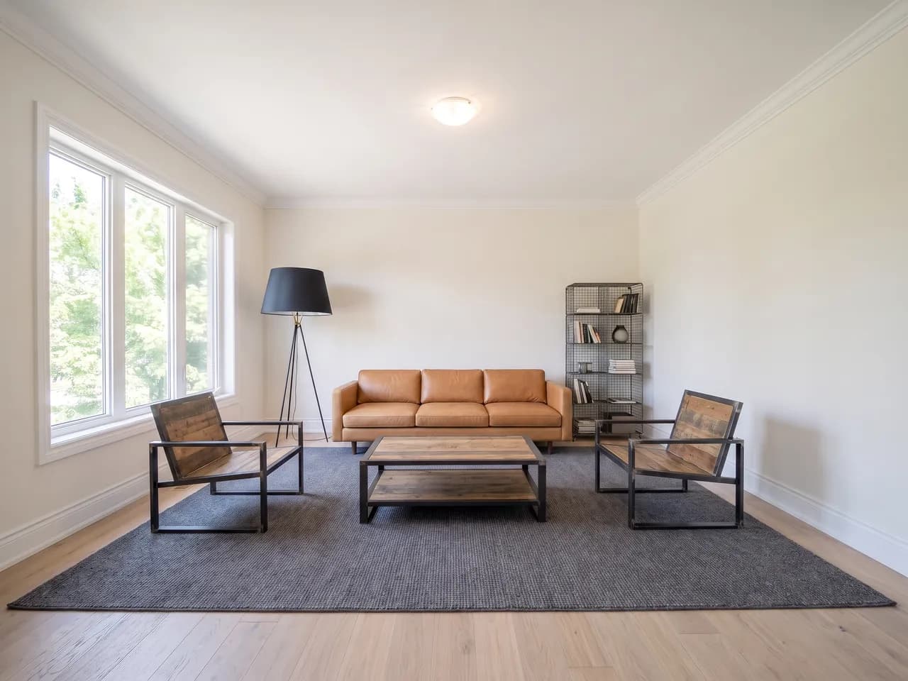 The same living room staged with a tan leather sofa, blackened steel furniture and wire shelving
